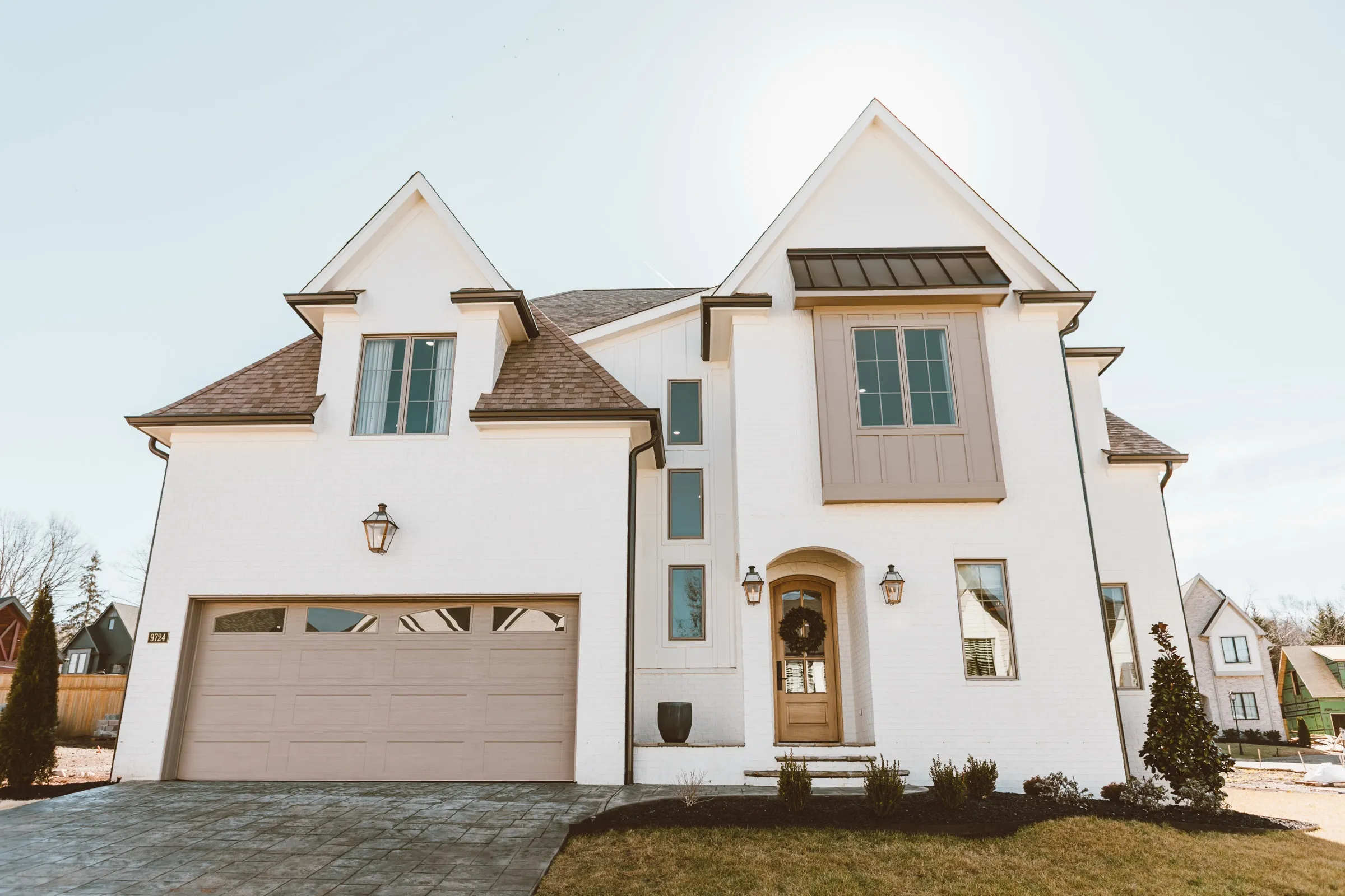 White painted-brick home with a tan garage door and gas lanterns